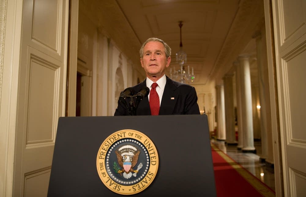 U.S. President George W. Bush addresses the nation from the Oval Office in 2008, delivering a primetime speech on the unfolding subprime mortgage and economic crisis. The photo shows him seated behind the Resolute Desk, looking directly into the camera.